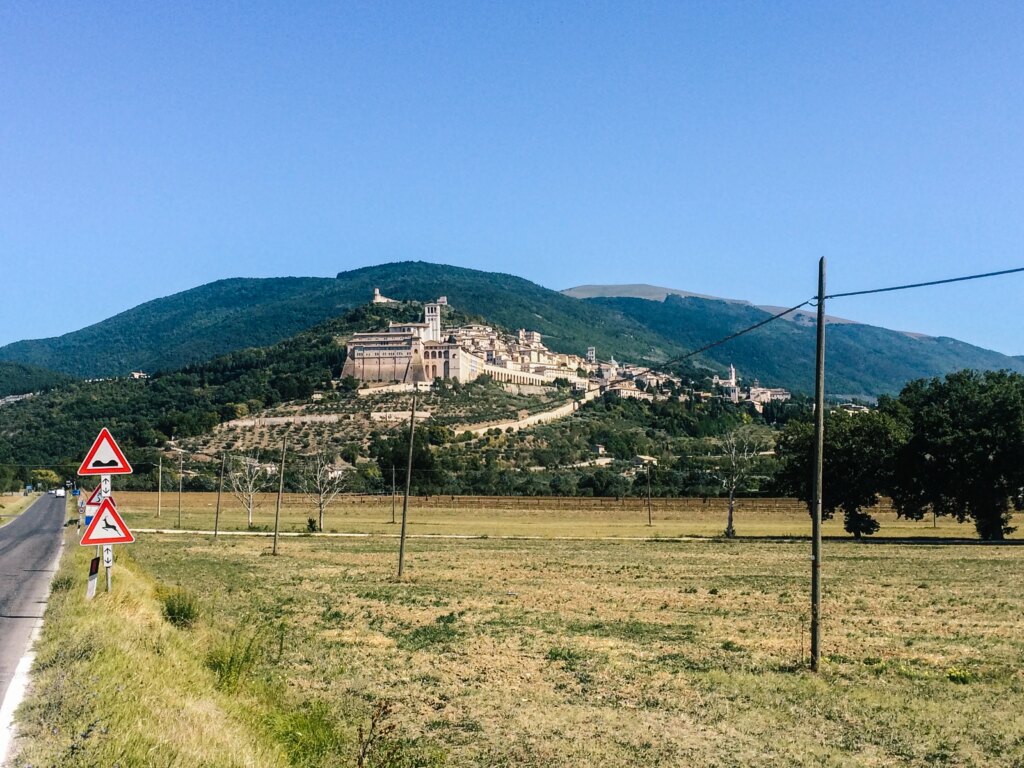 Panoramic view of Assisi with fields and green hills under a clear sky.